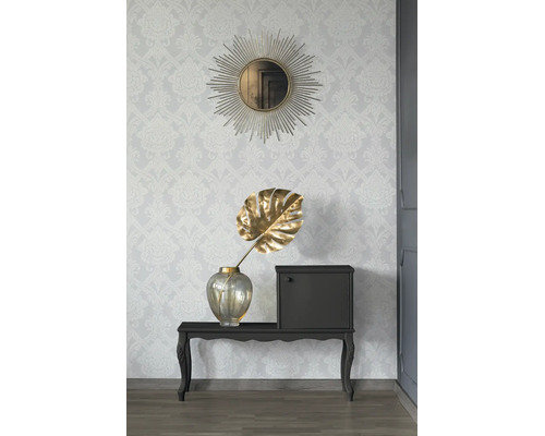 Vliesbehang met damastpatroon op een muur met een ronde zonnespiegel, consoletafel en een vaas met decoratieblad.