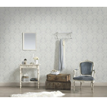 Vliesbehang met licht barokpatroon in een woonkamer met consoletafel, wandspiegel, stapel koffers en klassieke fauteuil.