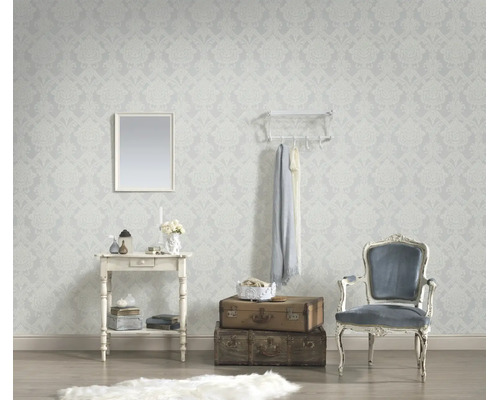 Vliesbehang met licht barokpatroon in een woonkamer met consoletafel, wandspiegel, stapel koffers en klassieke fauteuil.