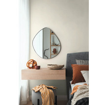 Moderne slaapkamer met een asymmetrische, organisch gevormde wandspiegel boven een zwevend houten console naast een gestoffeerd bed.