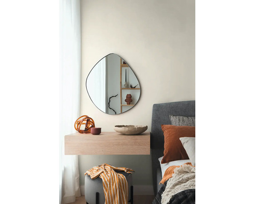 Moderne slaapkamer met een asymmetrische, organisch gevormde wandspiegel boven een zwevend houten console naast een gestoffeerd bed.