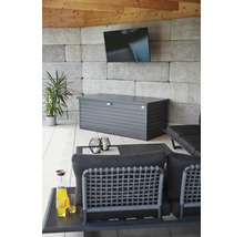 Metalen opbergbox in antraciet in een moderne loungehoek met stenen wand, televisie en tuinmeubels.