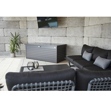 Metalen kussenkast op een licht terras met loungebank, bijzettafel, een plant en een muur van steenblokken.