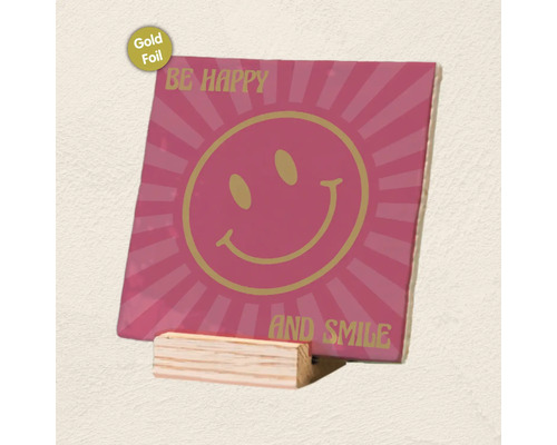 Decoratieve tegel met smiley, goudfolie-accenten en tekst Be Happy and Smile op een houten standaard.