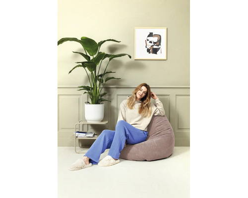 Lichte woonkamer met lambrisering, een grote kamerplant in een witte pot en een vrouw op een zitzak met textuur.