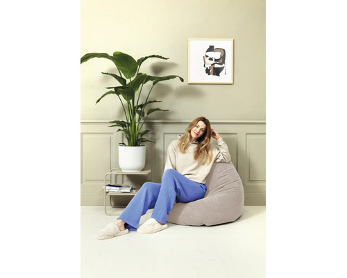 Vrouw zit op een comfortabele, ronde zitzak in een modern ingerichte woonkamer met kamerplant en wanddecoratie.