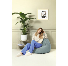 Een vrouw zit op een blauwe zitzak in een lichte, moderne kamer met een grote kamerplant en een abstract schilderij.