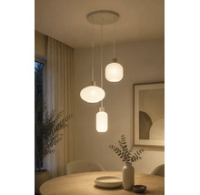 Drielichts hanglamp met wit geribbelde glazen kappen in diverse vormen boven een houten eettafel.
