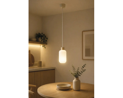 Moderne hanglamp met cilindrische glazen kap boven een ronde houten tafel in een minimalistisch ingerichte kamer.