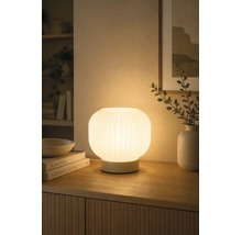 Verlichte tafellamp van geribbeld glas op een houten dressoir, zorgt voor een warme sfeer in de woonkamer.