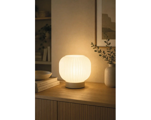 Verlichte tafellamp van geribbeld glas op een houten dressoir, zorgt voor een warme sfeer in de woonkamer.