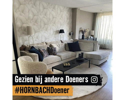 Modern ingerichte woonkamer met een lichte hoekbank, fauteuil, behang met bladmotief, rond vloerkleed, zwarte salontafel en Instagram Logo.