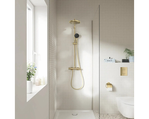 Moderne badkamer met messing douchesysteem, glazen douchewand, beige mozaïektegels en hangend toilet.