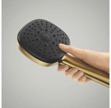 Een hand houdt een vierkante handdouche in goudkleur vast met een zwarte sproeikop en antikalknoppen.