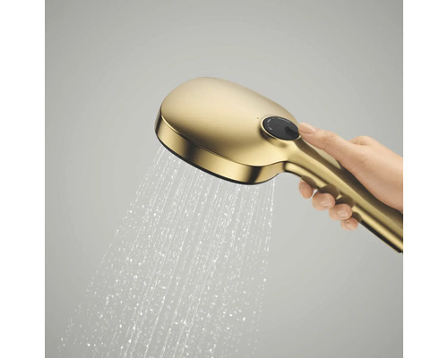 Een hand houdt een goudkleurige handdouche in werking vast waar water uit stroomt, met een drukknop aan de bovenkant.