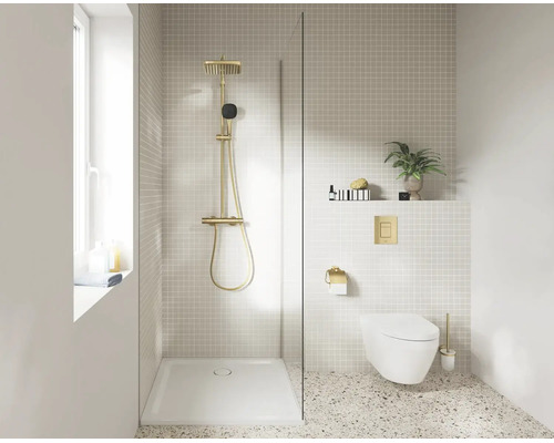 Moderne badkamer met inloopdouche, gouden regendouche, witte douchebak, hangend toilet met gouden bedieningsplaat en lichte terrazzovloer.