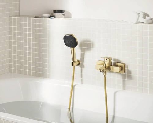 Goudkleurige badmengkraan met handdouche gemonteerd op een betegelde wand boven een wit bad.