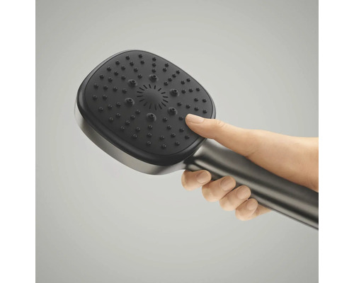 Een hand houdt een moderne, afgeronde vierkante handdouche vast met een metallic greep en donkere straalplaat.