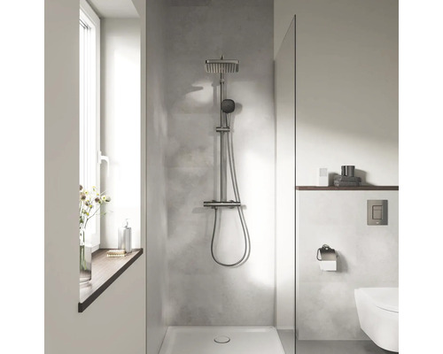 Moderne badkamer met douchesysteem inclusief hoofddouche en handdouche in een inloopdouche met betonlook wand en glazen douchewand.