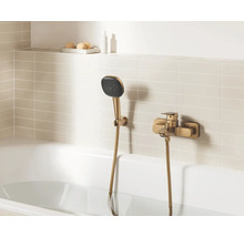 Moderne badmengkraan in brons-optiek met handdouche en houder, gemonteerd op een licht betegelde muur boven een wit ligbad.