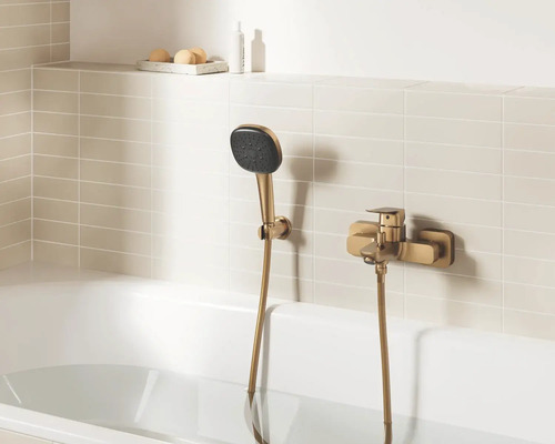 Moderne badmengkraan in brons-optiek met handdouche en houder, gemonteerd op een licht betegelde muur boven een wit ligbad.