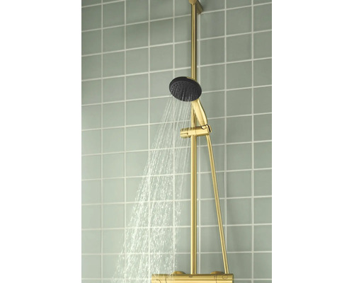 Goudkleurig douchesysteem met stromende handdouche op een betegelde wand.