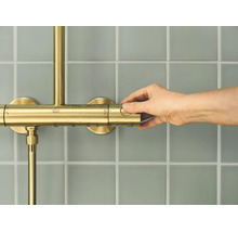 Hand bedient een Grohe douchethermostaat op een betegelde muur.