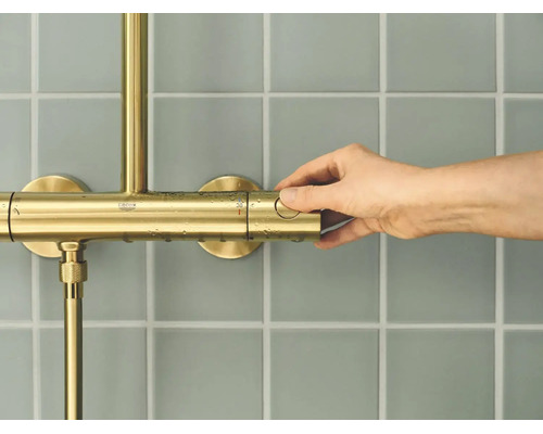 Hand bedient een Grohe douchethermostaat op een betegelde muur.