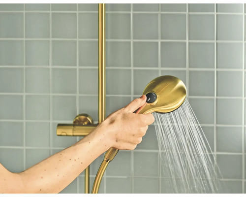 Hand houdt een handdouche met straalregelaar vast waar water uit stroomt, voor een betegelde wand.