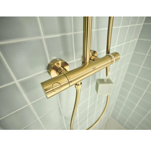 Grohe douchethermostaat in geborsteld goud op een betegelde wand.