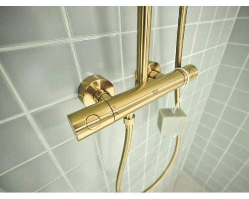 Grohe douchethermostaat in geborsteld goud op een betegelde wand.