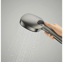 Een hand houdt een handdouche vast waar water uit spuit, met een ronde selectieknop op de achterkant.