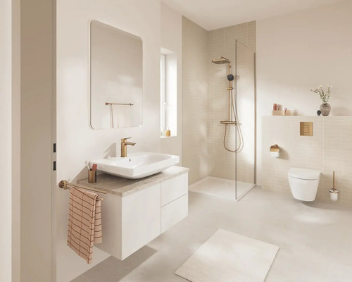 Lichte, moderne badkamer met wit wastafelmeubel, opbouwwastafel, gouden kraan, inloopdouche met glaswand en hangend toilet.