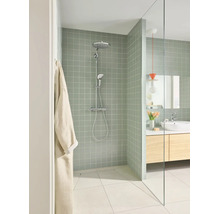 Moderne badkamer met inloopdouche, lichtgroene tegels, chromen douchesysteem, glazen wand en houten wastafelmeubel.