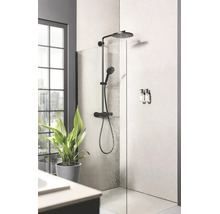 Moderne badkamer met inloopdouche, zwart douchesysteem met regendouche en handdouche, glazen douchewand en een groene plant.