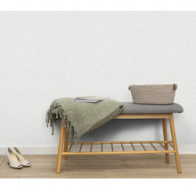 Gestructureerd vliesbehang op een muur met een houten bank, een deken, boeken en een mand in een lichte woonkamer.