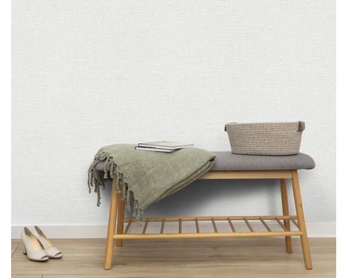 Gestructureerd vliesbehang op een muur met een houten bank, een deken, boeken en een mand in een lichte woonkamer.