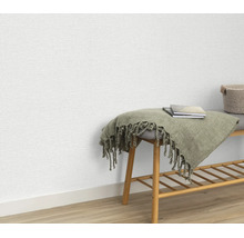 Gestructureerd vliesbehang aan een muur met een houten bankje en een deken als decoratie.
