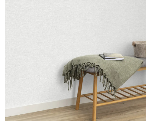 Gestructureerd vliesbehang aan een muur met een houten bankje en een deken als decoratie.