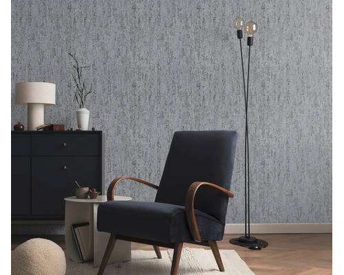 Woonkamer met vliesbehang in betonlook, fauteuil, dressoir en vloerlamp in een moderne interieurstijl.