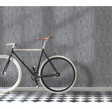 Een muur met gestructureerd vliesbehang in betonlook, ervoor staat een fiets op een vloer met zwart wit tegelpatroon.