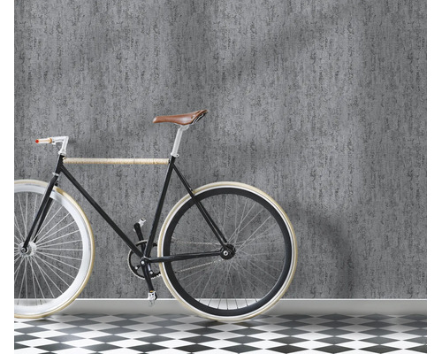 Een muur met gestructureerd vliesbehang in betonlook, ervoor staat een fiets op een vloer met zwart wit tegelpatroon.