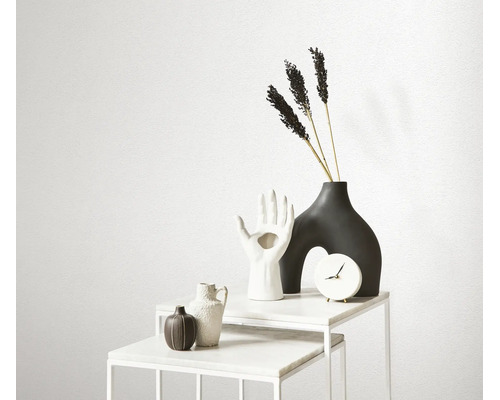 Decoratieve objecten op een witte marmeren tafel met klok, vazen in de vorm van een hand en abstracte vorm, en gedroogde bloemen.