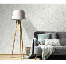 Woonkamer met vliesbehang met bladmotief, grijze bank, houten vloerlamp en woonaccessoires in een gezellig en modern interieur.