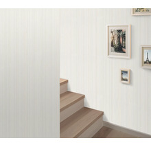 Vliesbehang met subtiel verticaal streepmotief in een hal met een houten trap en fotolijsten aan de wand.