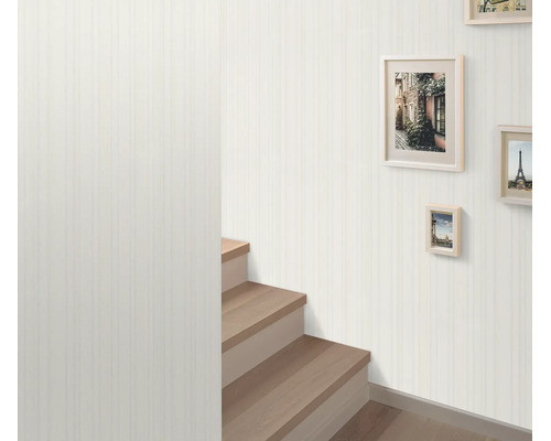 Vliesbehang met subtiel verticaal streepmotief in een hal met een houten trap en fotolijsten aan de wand.
