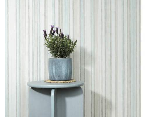 Vliesbehang met verticaal streeppatroon tegen een muur met plant in een bloempot op een ronde bijzettafel.