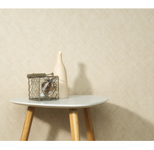 Gestructureerd behang met een fijn patroon geplaatst voor een muur met een kleine bijzettafel een vaas en een decoratief object in een draadmand.