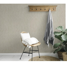 Woonkamer met gestructureerd vliesbehang, een rotan stoel met kussens, een houten kapstok en een kamerplant in een natuurlijke stijl.