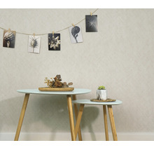 Woonruimte met gestructureerd behang, twee bijzettafels met houten poten en een fotolijn met botanische zwart-wit motieven aan de muur.